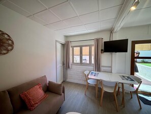 Une pièce comprenant un canapé, une table avec des chaises, un téléviseur et une fenêtre avec des rideaux.