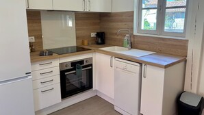 A compact kitchen with white cabinets, a built-in oven, a dishwasher, a coffee maker, and a window with a view of the outside.