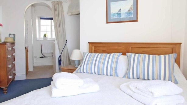 Una cama bien hecha con almohadones a rayas y toallas dobladas, un cabecero de madera y un cuadro en la pared.