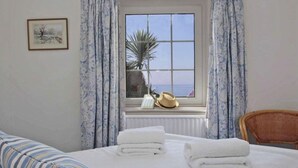 A hotel room with a bed, a window with curtains, a framed picture on the wall, and a chair. - Watchtower (Torpoint)