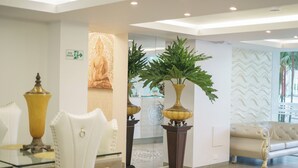 Un vestíbulo de hotel con una mesa de vidrio, sillas blancas, un sofá y plantas decorativas.