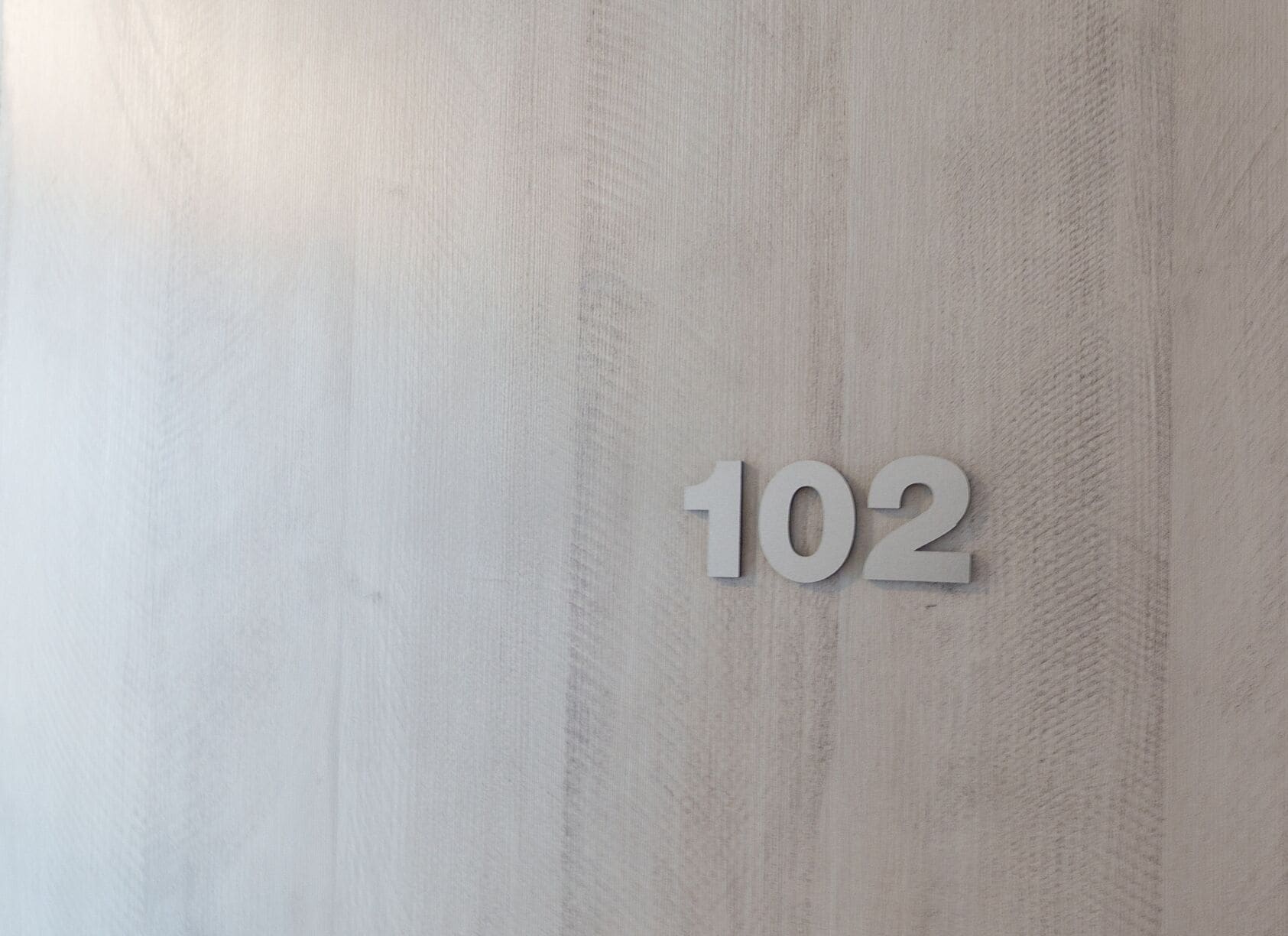 Un mur à la surface texturée, sur lequel est inscrit le chiffre « 102 » dans une police de caractères minimaliste.