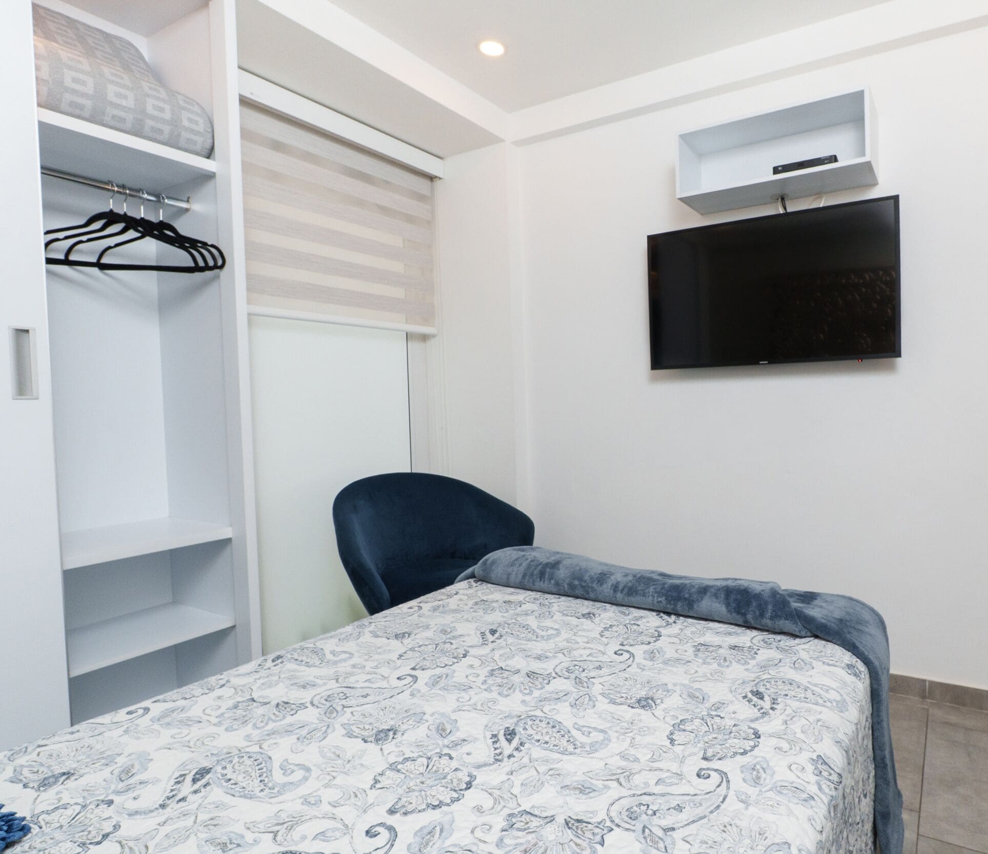 A bedroom with a bed, a chair, a wardrobe, and a TV.