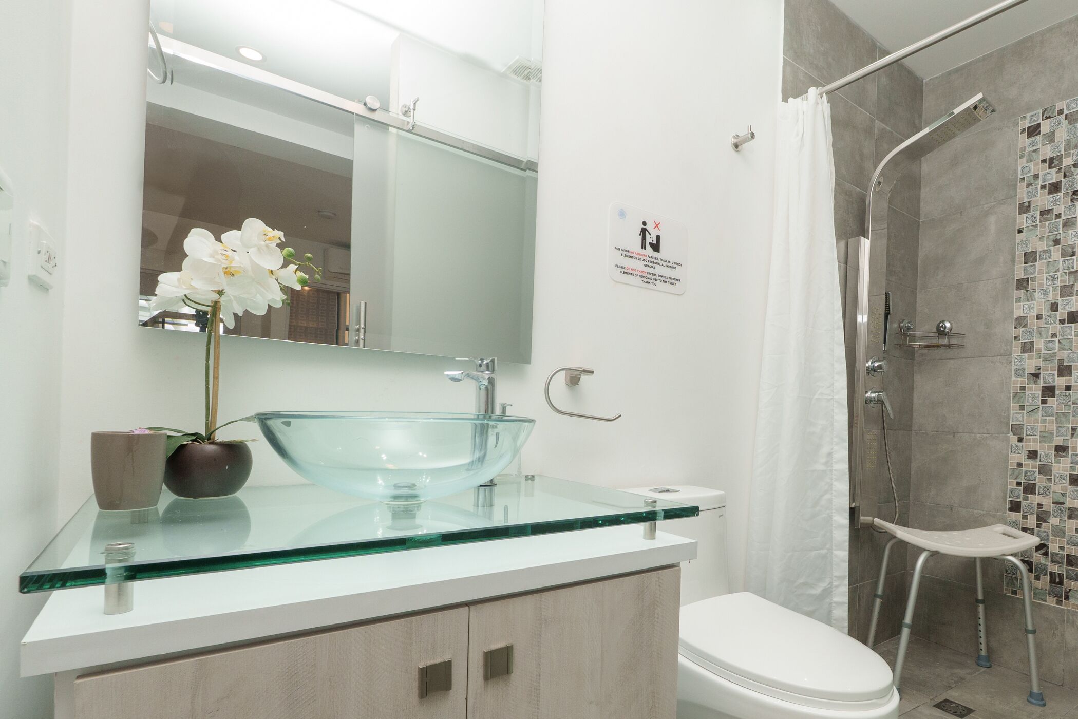 Un bagno moderno con un lavandino in vetro, un water bianco e una zona doccia.