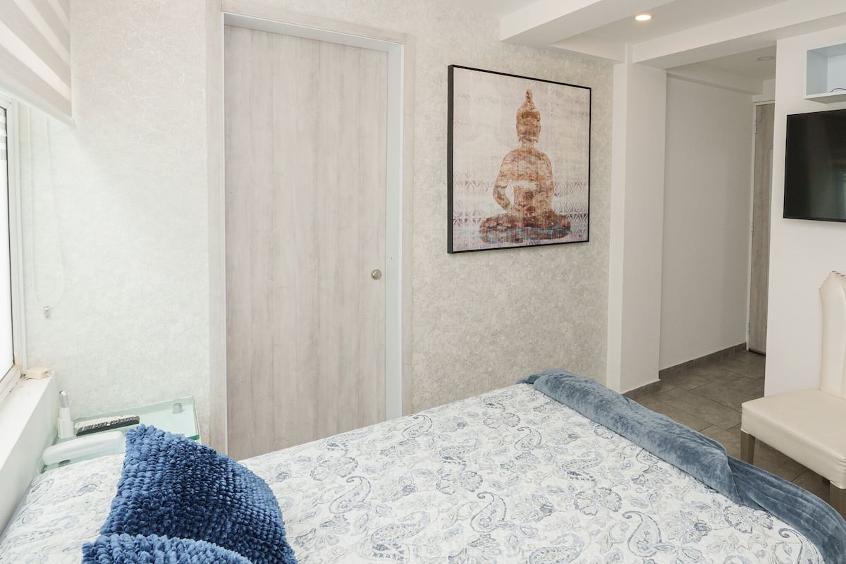 Quarto com cama, porta, quadro pendurado na parede e televisão na parede.