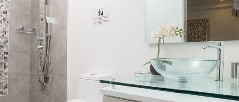 Un baño moderno con lavabo de vidrio, inodoro y zona de ducha.