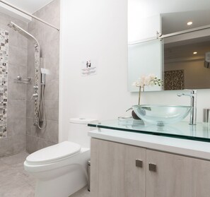 Bathroom features a glass vessel sink, curved glass shower door, and a large mirror.