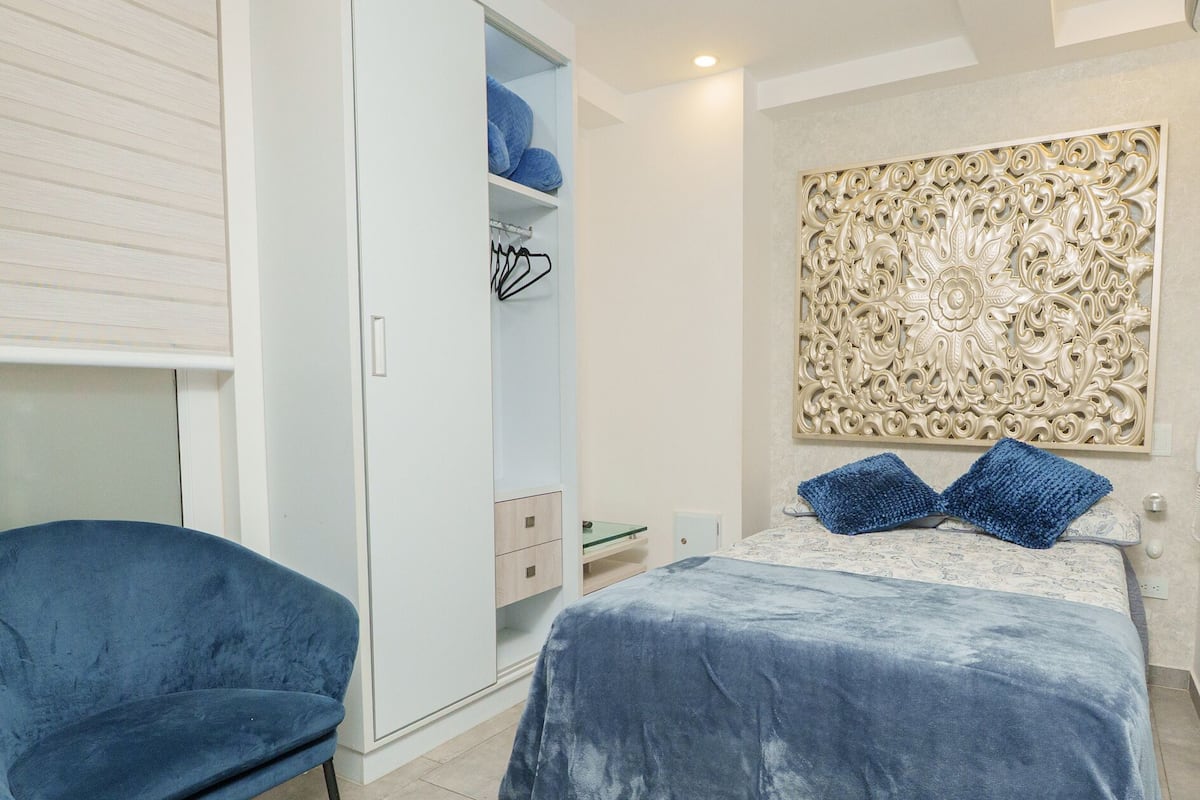 Quarto com cama, guarda-roupa, cadeira e um painel decorativo na parede.