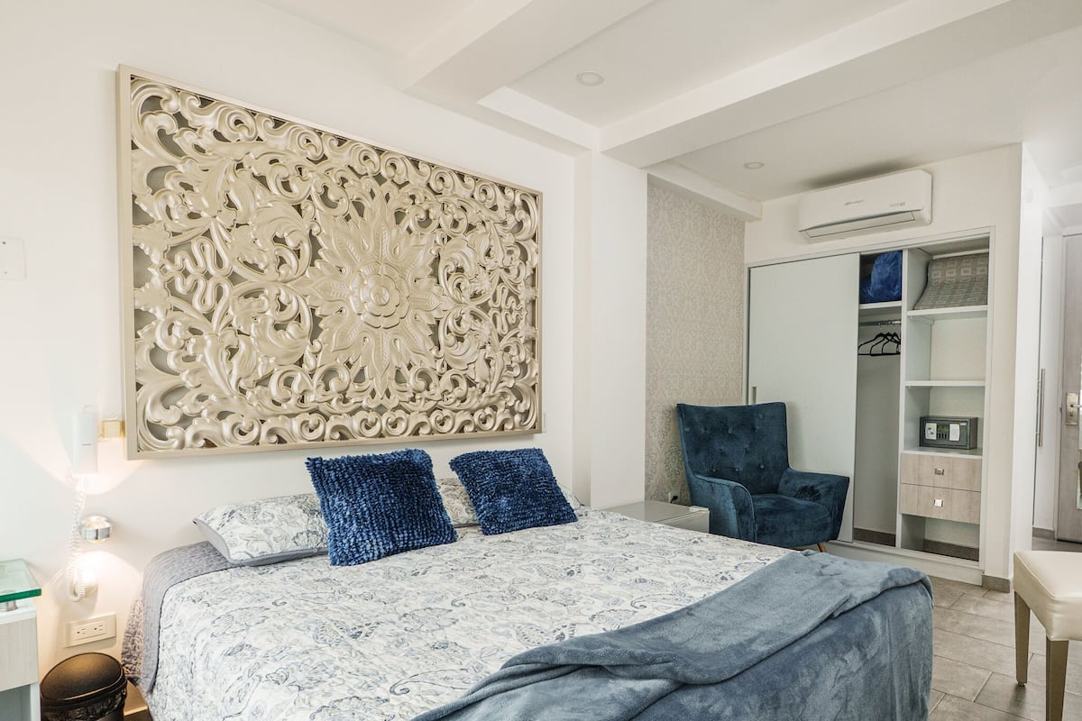 Quarto com cama, painel decorativo, guarda-roupa e ar condicionado.