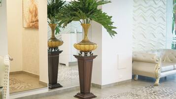 A reception area with a large mirror, a Buddha statue, two potted plants, a patterned rug, and a white sofa.