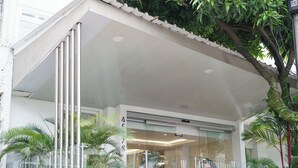 Un edificio moderno con entrada de vidrio, paredes exteriores blancas y un balcón con barandillas de metal.