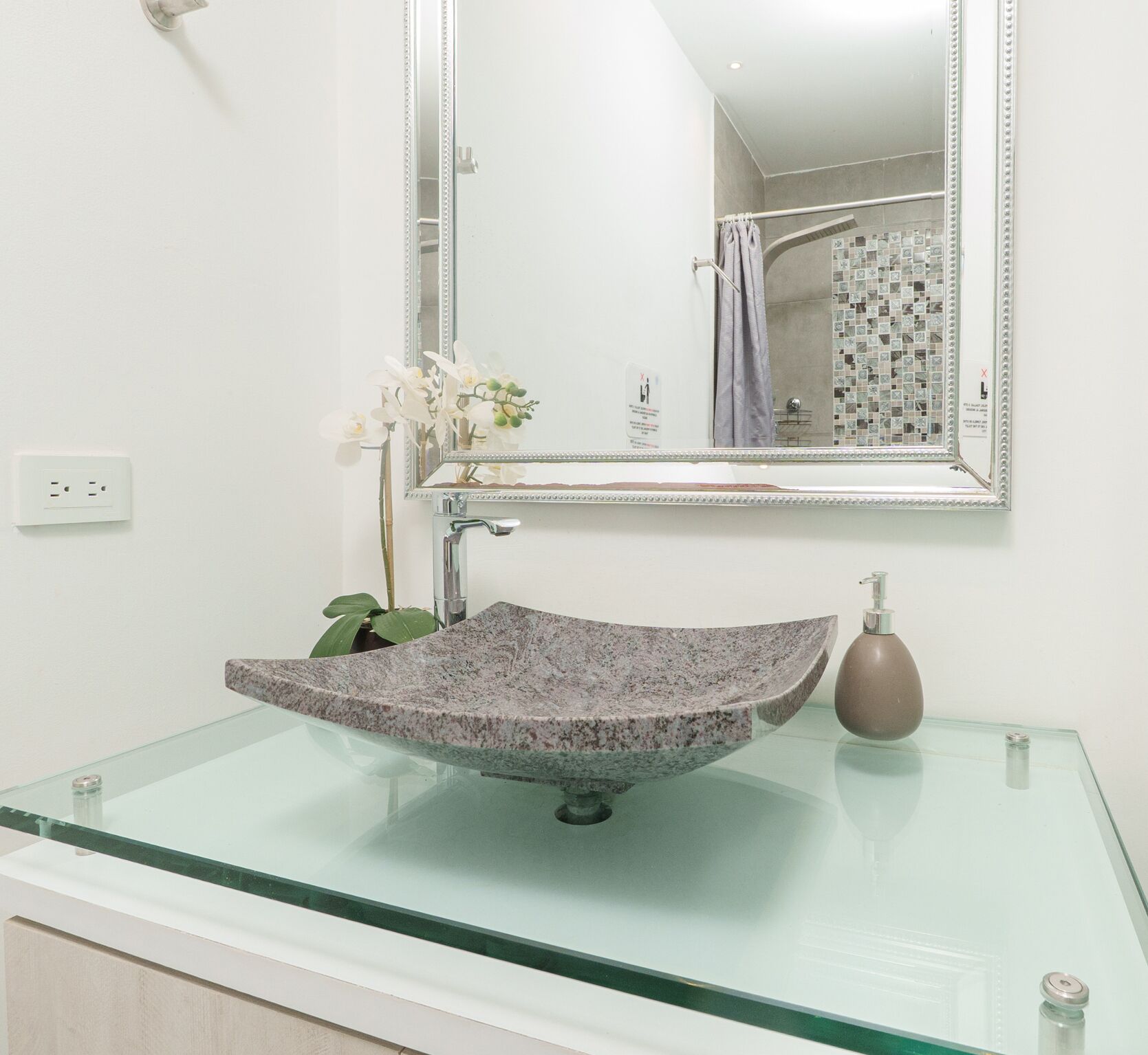 Une salle de bain dotée d’un lavabo en verre, d’un receveur en marbre, d’un grand miroir et d’un espace douche avec un mur carrelé.