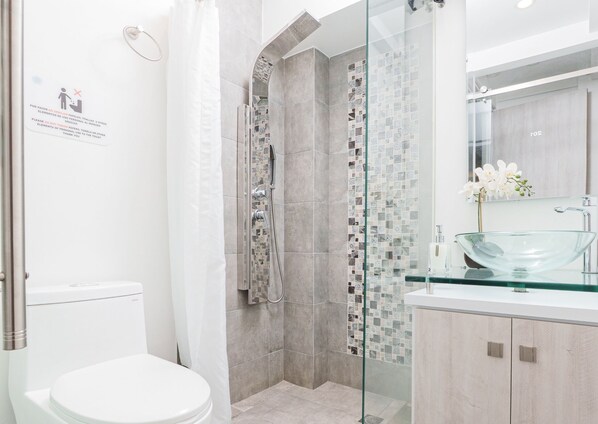 Ein modernes Badezimmer mit einer gläsernen Dusche, einer weißen Toilette und einem Waschbecken aus Glas mit Holzschrank.