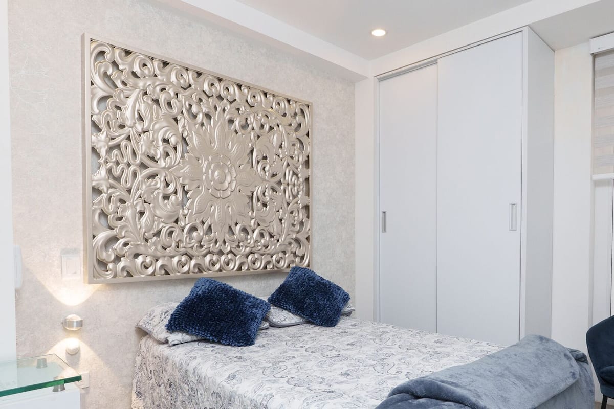 Quarto com cama, painel decorativo, guarda-roupa e mesa de cabeceira com abajur.