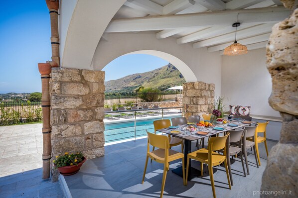 An outdoor dining area with a pool view, stone pillars, and yellow chairs.