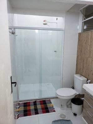 Ein Badezimmer mit Duschkabine aus Glas, Toilette, Waschbecken und Mülleimer.