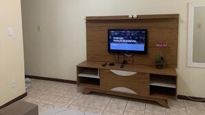 A living room with a wooden entertainment center, a flat-screen TV, and a potted plant. - Centro da Cidade 2 quartos cama de casal (Cabo Frio)