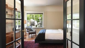 A bedroom with a bed, a chair, a window, and a door with glass panels. - Classic Bright Modern Spacious 1bd/1ba Apartment (Berkeley)