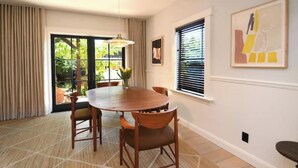 A dining area with a round wooden table, four chairs, a hanging light fixture, a window with blinds, and a framed abstract painting on the wall. - Classic Bright Modern Spacious 1bd/1ba Apartment (Berkeley)