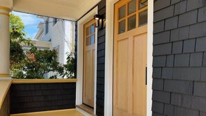 A covered porch with dark siding and a light-colored floor, leading to a wooden door with glass panels. - Classic Bright Modern Spacious 1bd/1ba Apartment (Berkeley)