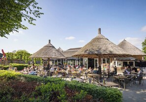 An outdoor café with thatched-roof tables and chairs, surrounded by greenery. - Camping Marvilla Parks Kaatsheuvel (Kaatsheuvel)