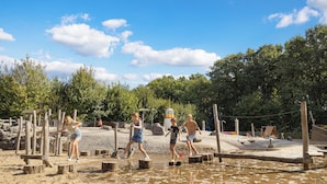 Ein Sandstrand mit Holzstegen und einem Spielplatz im Hintergrund.
