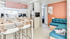 Eine moderne Küche mit weißen Schränken, ein Essbereich mit Barhocker und ein Wohnbereich mit einem türkisfarbenen Sofa.