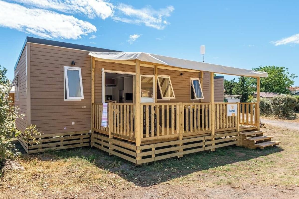 Une maison mobile en bois dotée d’une véranda, d’un espace extérieur couvert et d’une petite terrasse.