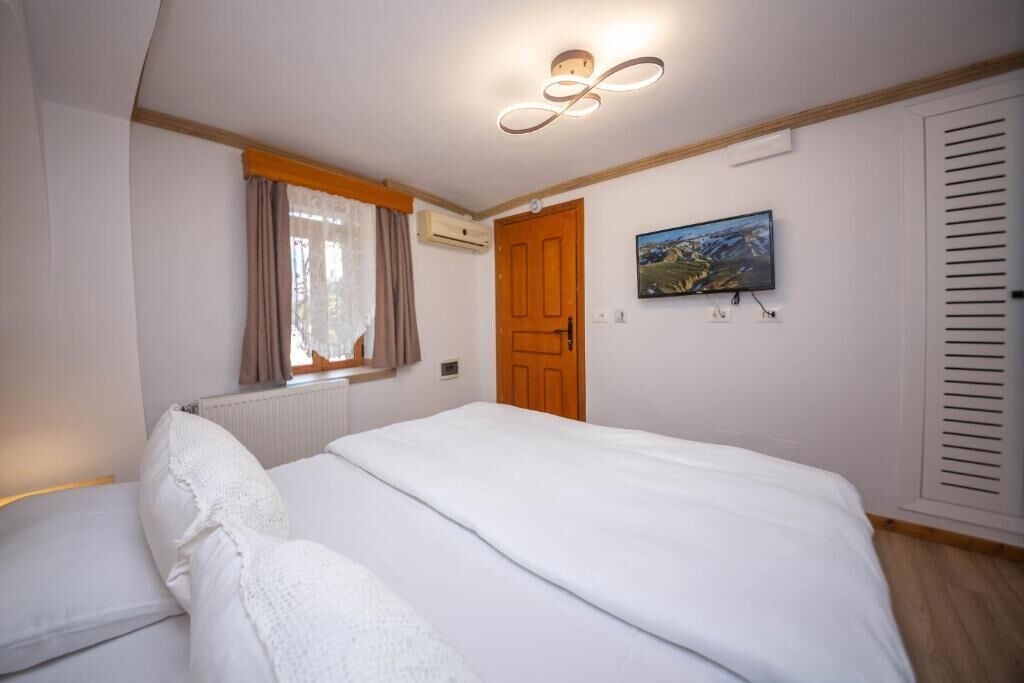 Un dormitorio con cama, ventana con cortinas, aire acondicionado, puerta de madera, televisor montado en la pared y radiador.