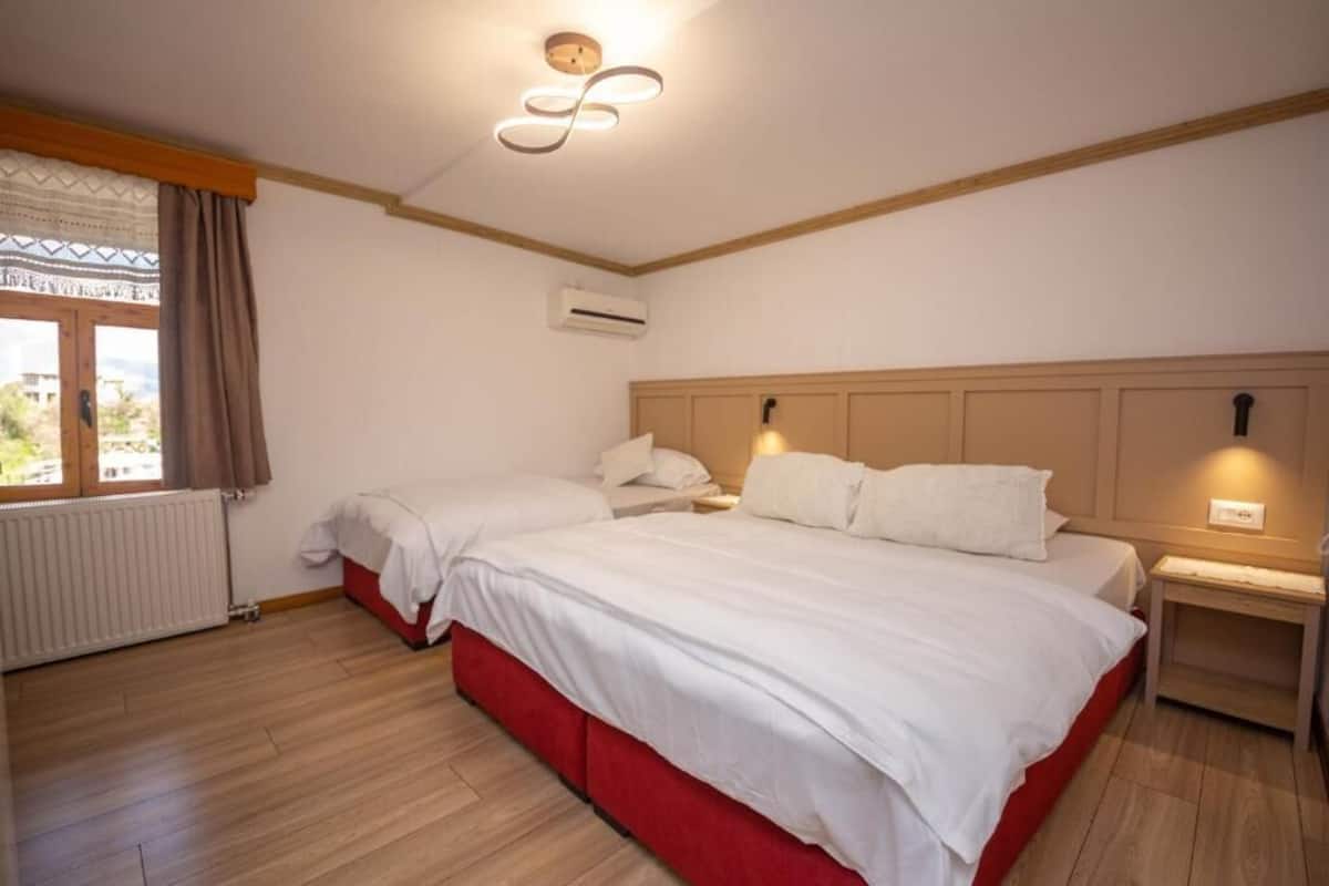 A bedroom with two beds, a wooden floor, a window with curtains, an air conditioning unit, and a ceiling light fixture.