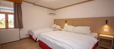 A bedroom with two beds, a wooden floor, a window with curtains, an air conditioning unit, and a ceiling light fixture.