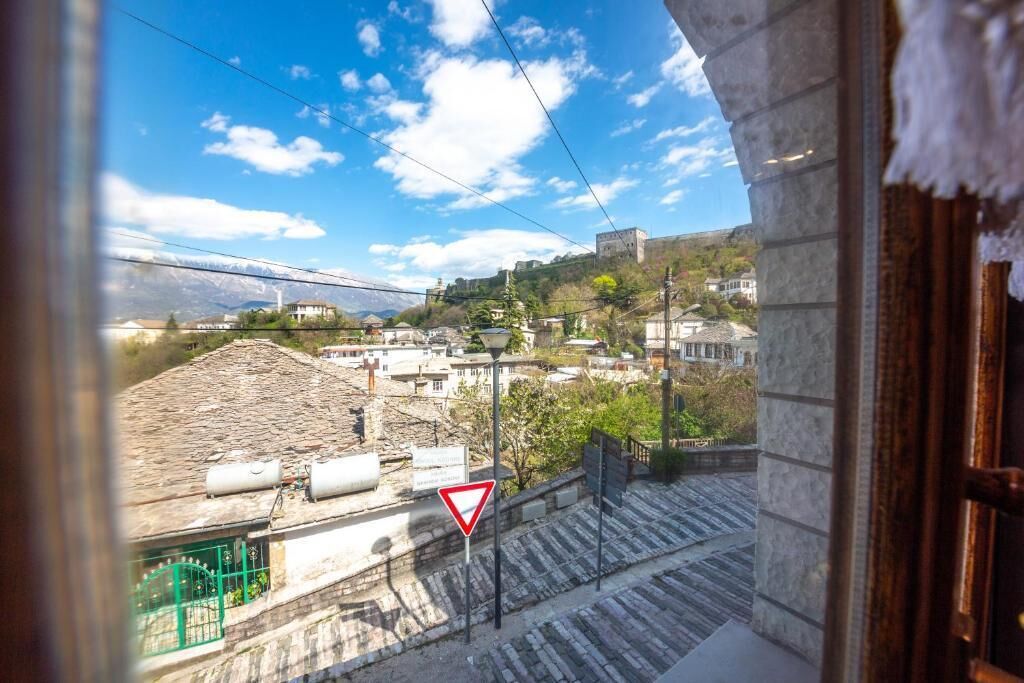 A view from a window overlooking a town with buildings, a triangular warning sign, and a clear sky.
