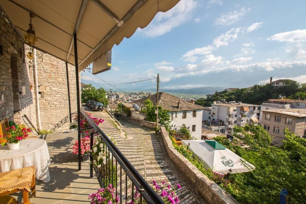 Uma varanda com parede de pedra, uma mesa com uma cadeira e vista para uma cidade com edifícios e áreas verdes.