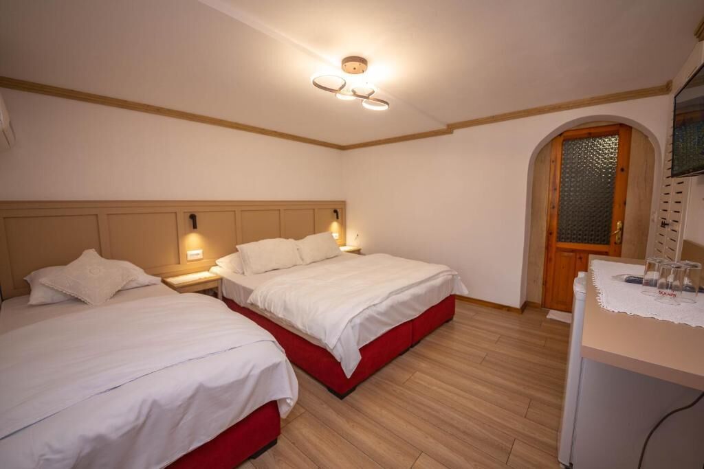 A hotel room with two beds, a wooden floor, a small desk with a lamp, and a door with a glass panel.