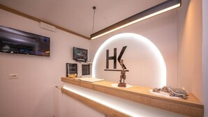 A reception desk with a large illuminated 'HK' sign, a flat-screen TV, and a small statue. - Bed and Breakfast Kotoni (Gjirokastër)