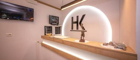 A reception desk with a large illuminated 'HK' sign, a flat-screen TV, and a small statue.