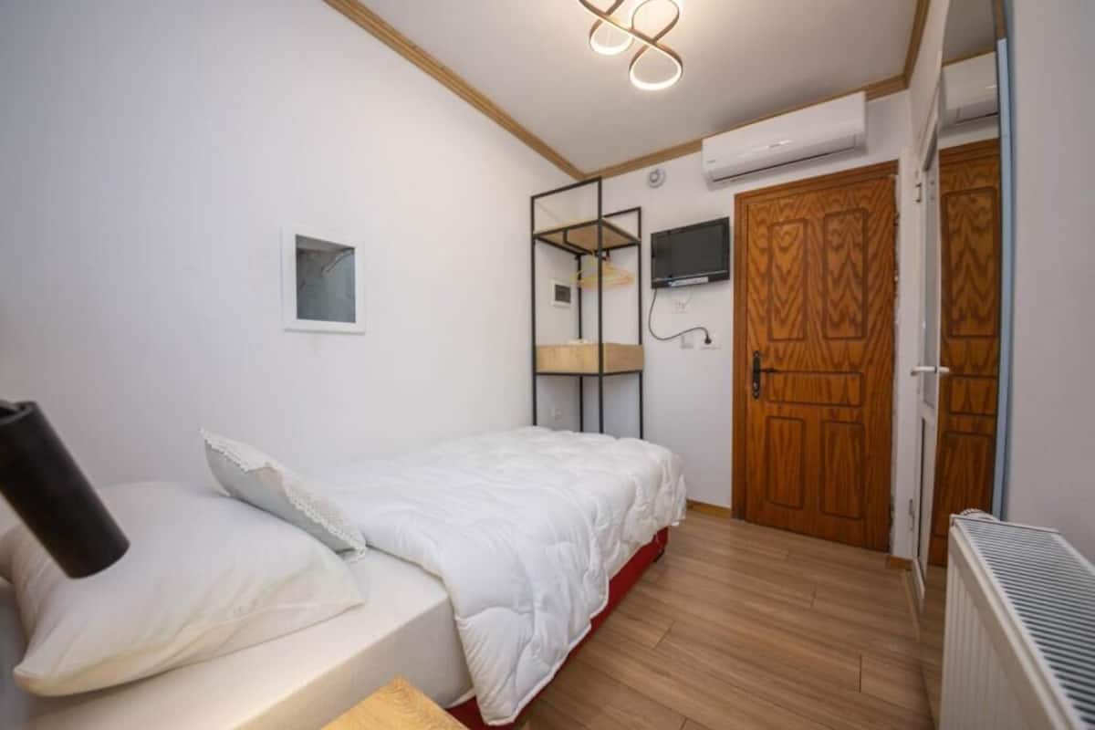 A bedroom with a bed, a small bedside table, a wall-mounted TV, and a wooden wardrobe.