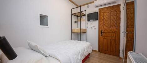 Ein Schlafzimmer mit einem Bett, einem kleinen Nachttisch, einem an der Wand montierten Fernseher und einem Holzschrank.