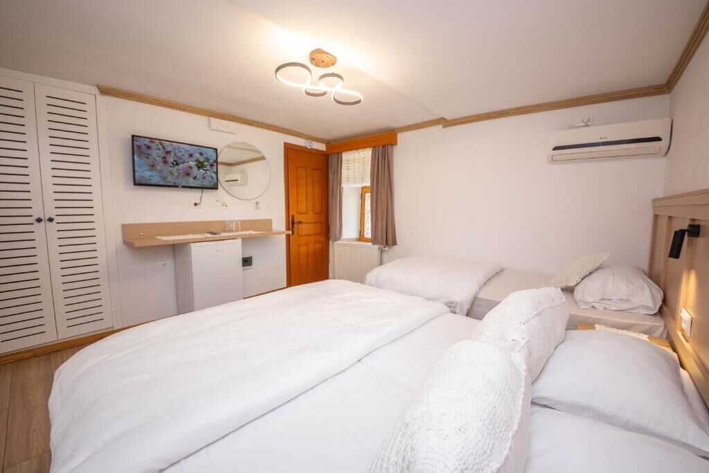 A bedroom with two beds, a wooden wardrobe, a small desk, a mirror, and an air conditioning unit.