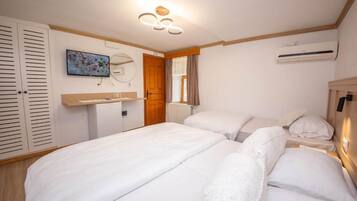 A bedroom with two beds, a wooden wardrobe, a small desk, a mirror, and an air conditioning unit.