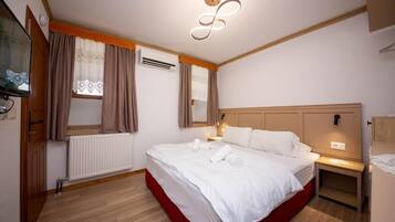 Quarto de hotel com uma cama grande, cabeceira de madeira, mesa de cabeceira, ar condicionado fixado na parede e uma janela com cortinas.