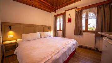 A bedroom with a wooden ceiling, a bed with white bedding, a nightstand, a window with curtains, and a radiator.