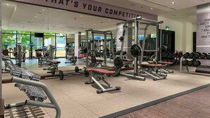Ein Fitnessstudio mit verschiedenen Trainingsgeräten, einem motivierenden Zitat an der Wand und einem großen Spiegel, der den Raum widerspiegelt.