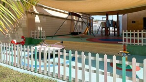 Ein Spielplatz mit Schaukeln, einer Rutsche und Klettergerüsten, umzäunt durch einen weißen Zaun.