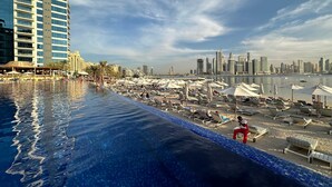 A poolside area with lounge chairs and umbrellas, a city skyline in the background, and a clear sky. - Upgraded 1BR Paradise With Private Garden - Oceana (Dubai)