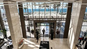 A modern hotel lobby with a glass entrance, a reception desk, and a view of the ocean. - Cozy Beachfront 1 Bedroom Apartment - The 8 (Dubai)