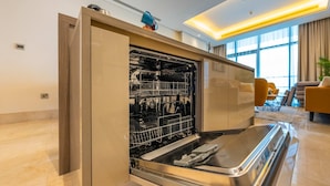 Een open vaatwasser in een moderne keuken met een marmeren aanrechtblad en uitzicht op een zithoek met een bank en een salontafel.