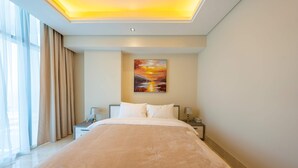 Een moderne hotelkamer met een groot bed, een nachtkastje, een lamp en een schilderij van een zonsondergang aan de muur.