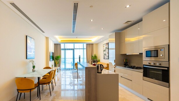 Een moderne keuken met een centraal eiland, roestvrijstalen apparatuur en een eethoek met gele stoelen.