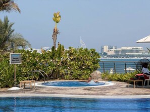 Zona de piscina amb un cartell que indica un límit d'edat, envoltada de vegetació exuberant i una vista d'un paisatge urbà amb arquitectura singular.